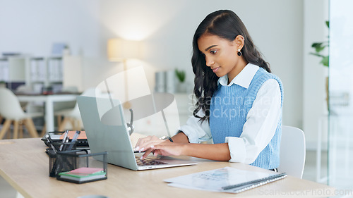 Image of Young woman happily doing business and networking by email on laptop. Professional female is stylish and creative while being alone in office. She is using technology to advance her career