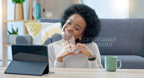 Image of Woman making a heart gesture and talking on video call with a tablet at home. Young female calling and greeting her boyfriend or husband, using wireless technology to connect with loved ones