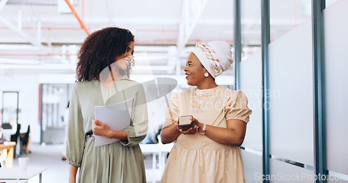 Image of Business team, talking and walking together for communication, gossip or happy conversation while working at a coworking office. Black women with a phone and paperwork while sharing ideas and advice