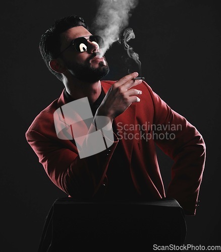 Image of Fashion, smoke and red with a man model in studio on a dark background wearing a suit for style. Smoking, mafia and edgy with a handsome young male posing on black space holding a cigarette