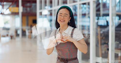 Image of Face, heart and business woman with hand sign in office building, smile and happy for startup success. Asian girl, hand and emoji icon by excited business owner smiling for company vision in Japan