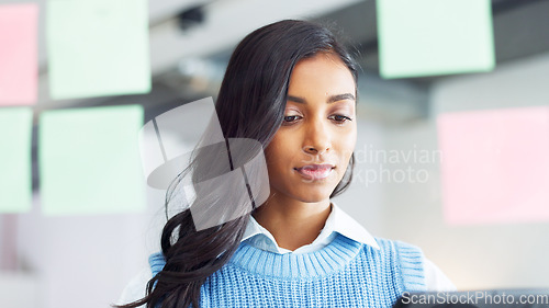 Image of Focused young business woman thinking while brainstorming solutions for a project and marketing strategy in a creative startup agency. Designer planning ideas and information on a window in an office