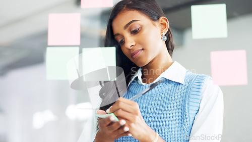 Image of Young business woman brainstorming and planning a mind map while writing ideas on sticky notes on a glass wall in an office. Focused designer analyzing a marketing strategy and solutions for projects