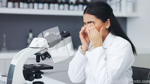 Image of Female scientist looking through microscope and rubbing her eyes while suffering from eye strain or discomfort. Stressed biotechnology specialist does analysis of test sample in medical lab