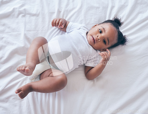 Image of Baby, portrait and girl on a bedroom bed feeling relax and calm in a nursery after rest. Young newborn, child and kid with a diaper in the morning with wellbeing and childcare from above in a house