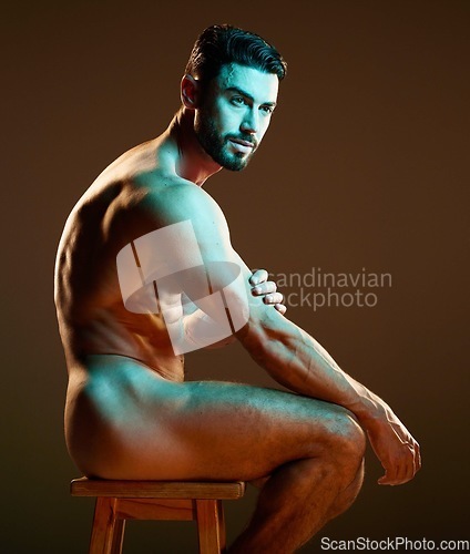 Image of Nude male model sitting, muscular body in neon lighting in studio with creative dark background. Sexy man posing on chair, side profile of naked person for artistic photography and night aesthetic