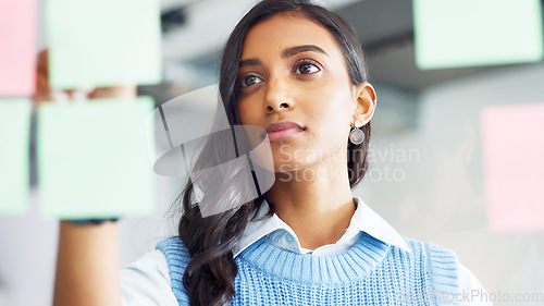 Image of Focused young business woman thinking while brainstorming solutions for a project and marketing strategy in a creative startup agency. Designer planning ideas and information on a window in an office