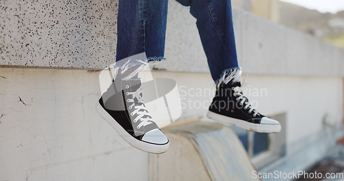 Image of Rooftop, shoes and man in an urban city sitting on the top of a building for a view of the cityscape. Hipster, freedom and closeup of male feet with sneakers hanging from an outdoor roof in town.