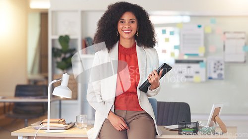 Image of Professional woman working on tablet device. Young female is in an office, sitting on a desk, smiling and busy with her job. As an accountant or lawyer, she is speaking to a client or coworker.