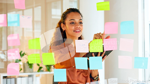 Image of Happy female designer planning ideas on a glass wall with colorful sticky notes inside a creative and modern office. Busy woman enjoying her job while brainstorming projects and managing projects