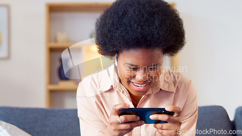 Image of Excited online gamer excited about winning successful mobile game while relaxing at home. Young stylish female enjoying some online entertainment using a mobile device on a sofa in her house
