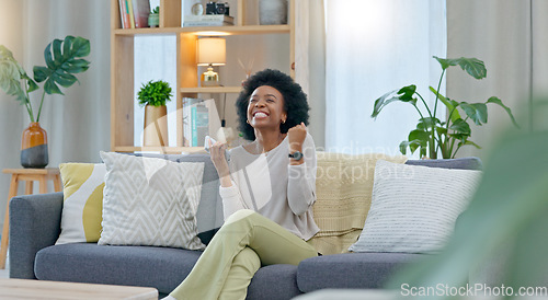 Image of African woman celebrating a new job while sitting at home on a couch. A young females loan is approved via an email on her phone. A happy and excited lady cheering for a promotion on a sofa
