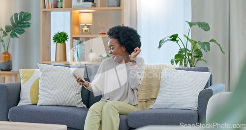 Image of African woman celebrating a new job while sitting at home on a couch. A young females loan is approved via an email on her phone. A happy and excited lady cheering for a promotion on a sofa