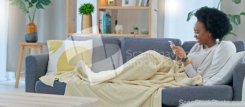 Image of Happy black woman reading social media gossip on phone while relaxing on a sofa at home. Young African American female texting and sharing an interesting scandal, shocked about drama on the internet