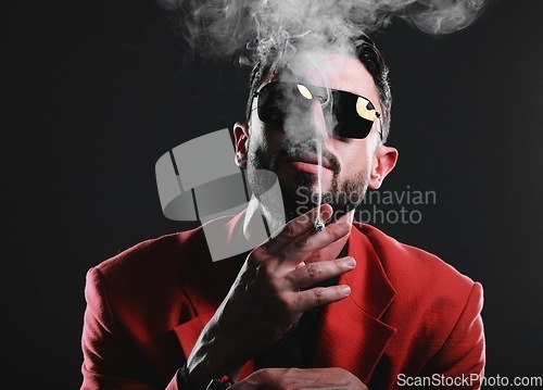 Image of Fashion, smoke and portrait with a man model in studio on a dark background wearing a suit for style. Smoking, mafia and edgy with a handsome young male posing on black space holding a cigarette