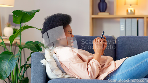 Image of A laughing young woman texting on a phone at home. Cheerful female chatting to her friends on social media, browsing online and watching funny internet memes while relaxing on a sofa