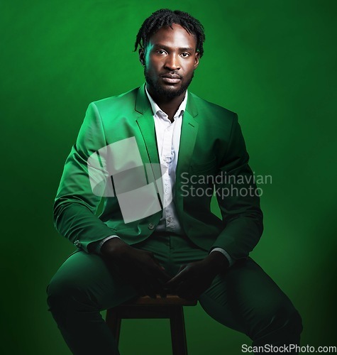 Image of Fashion, formal and portrait of a black man in a suit sitting on a chair in studio with a luxury outfit. Elegant, stylish and African male model with fashionable clothes isolated by green background.