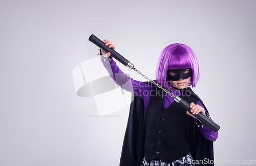 Image of Little girl, halloween and superhero dress up with nunchucks for fighting against a grey studio background. Portrait of isolated girl playing super hero with martial art karate weapon and purple hair