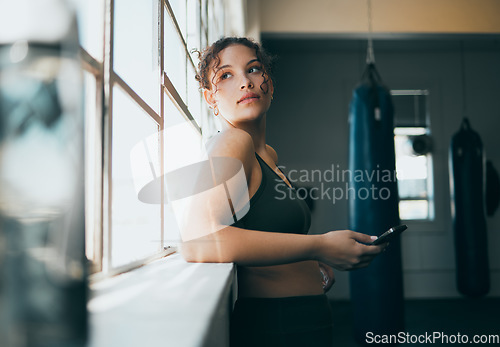 Image of Thinking, phone and fitness with a sports woman by a window, standing in the gym during an exercise workout. Health, idea and a female athlete using social media or an app to track her training