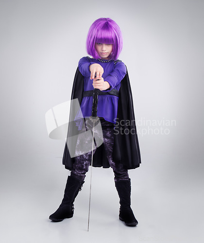 Image of Little girl, superhero and halloween dress up posing with sword against a grey studio background. Portrait of girl child playing super hero with purple hair, costume or cosplay of a warrior vigilante