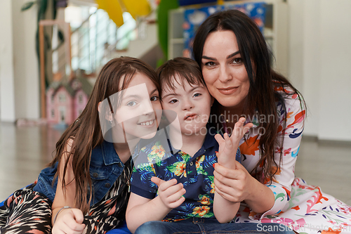 Image of A girl and a woman hug a child with down syndrome in a modern preschool institution