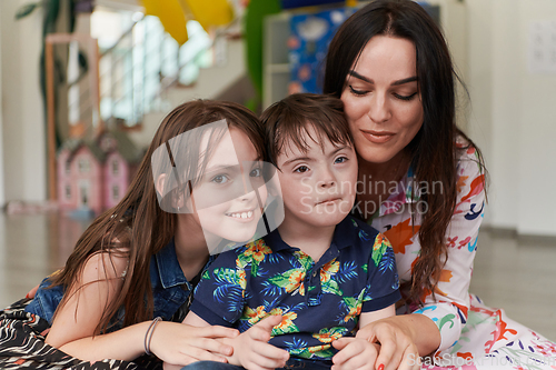 Image of A girl and a woman hug a child with down syndrome in a modern preschool institution