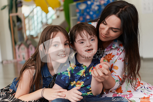 Image of A girl and a woman hug a child with down syndrome in a modern preschool institution