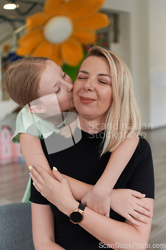 Image of A cute little girl kisses and hugs her mother in preschool