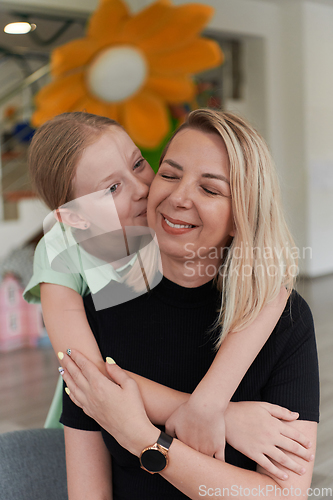 Image of A cute little girl kisses and hugs her mother in preschool