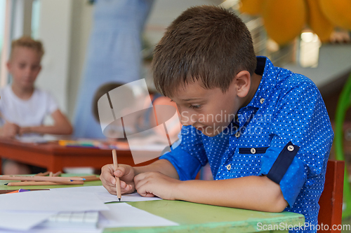 Image of A boy at a preschool institution sits and draws in a notebook with a smile on his face