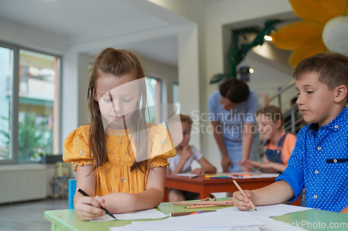 Image of Creative kids during an art class in a daycare center or elementary school classroom drawing with female teacher.