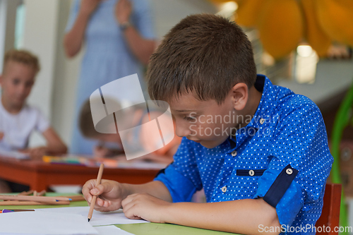 Image of A boy at a preschool institution sits and draws in a notebook with a smile on his face