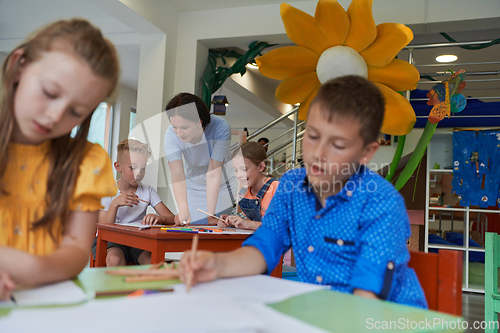 Image of Creative kids during an art class in a daycare center or elementary school classroom drawing with female teacher.