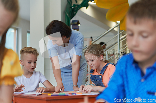 Image of Creative kids during an art class in a daycare center or elementary school classroom drawing with female teacher.