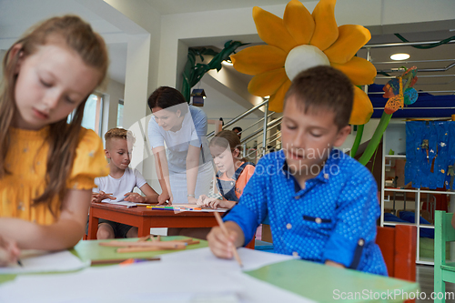 Image of Creative kids during an art class in a daycare center or elementary school classroom drawing with female teacher.