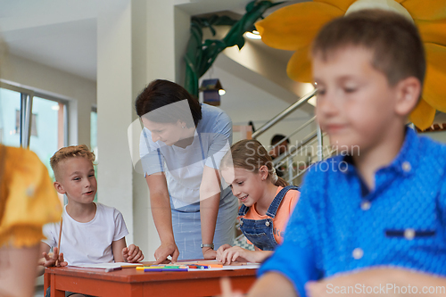 Image of Creative kids during an art class in a daycare center or elementary school classroom drawing with female teacher.