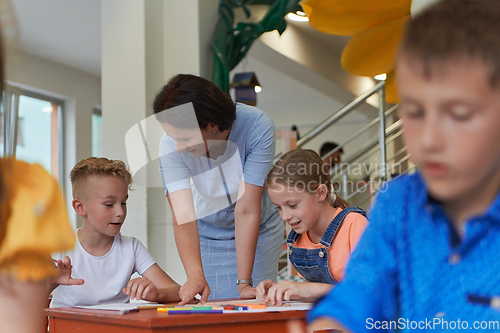 Image of Creative kids during an art class in a daycare center or elementary school classroom drawing with female teacher.