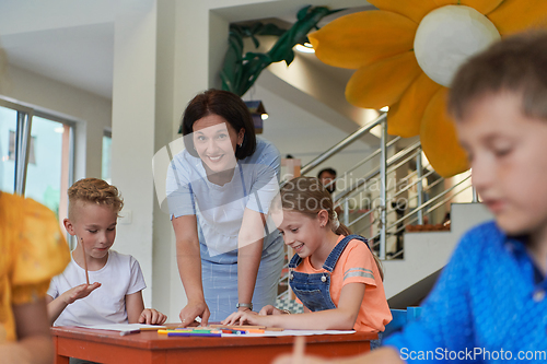 Image of Creative kids during an art class in a daycare center or elementary school classroom drawing with female teacher.