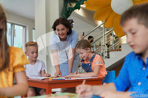 Image of Creative kids during an art class in a daycare center or elementary school classroom drawing with female teacher.