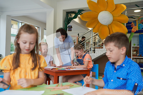 Image of Creative kids during an art class in a daycare center or elementary school classroom drawing with female teacher.