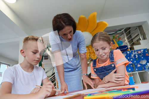 Image of Creative kids during an art class in a daycare center or elementary school classroom drawing with female teacher.