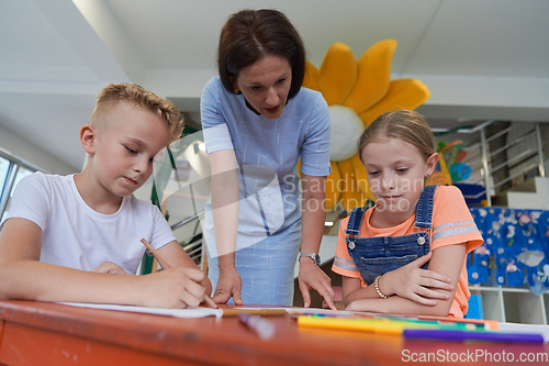 Image of Creative kids during an art class in a daycare center or elementary school classroom drawing with female teacher.