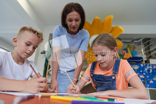 Image of Creative kids during an art class in a daycare center or elementary school classroom drawing with female teacher.