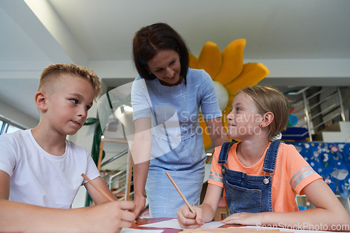 Image of Creative kids during an art class in a daycare center or elementary school classroom drawing with female teacher.