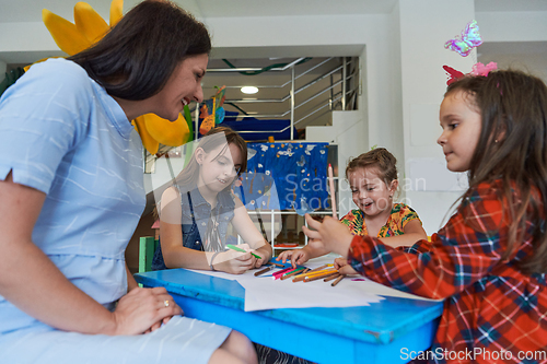 Image of Creative kids during an art class in a daycare center or elementary school classroom drawing with female teacher.