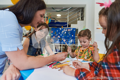 Image of Creative kids during an art class in a daycare center or elementary school classroom drawing with female teacher.