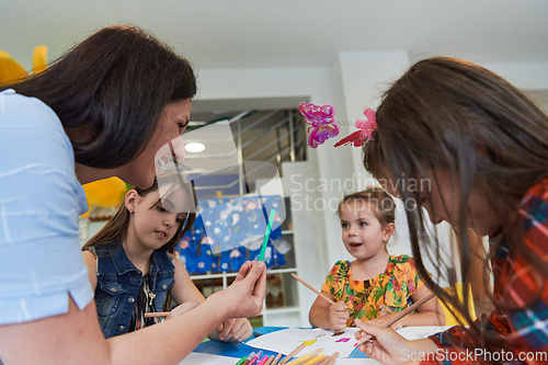 Image of Creative kids during an art class in a daycare center or elementary school classroom drawing with female teacher.