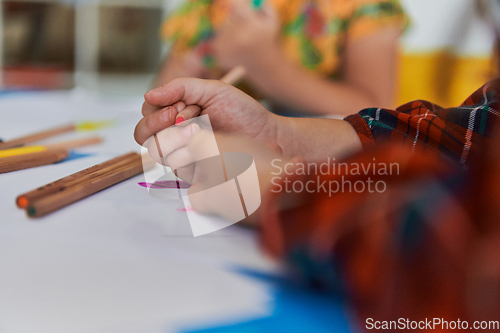 Image of Close up photo of kids during an art class in a daycare center or elementary school classroom drawing with female teacher.