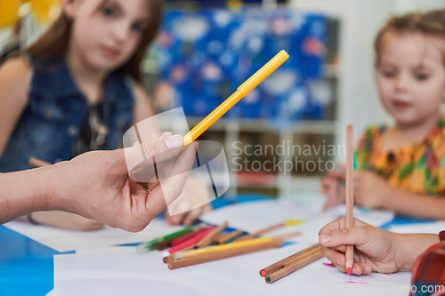 Image of Close up photo of kids during an art class in a daycare center or elementary school classroom drawing with female teacher.