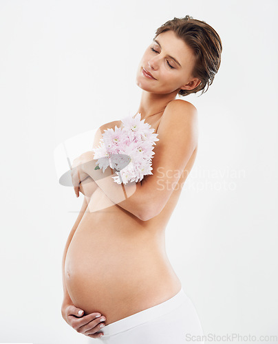 Image of Pregnancy, calm and woman with flowers in a studio holding her stomach with love, care and happiness. Feminine, maternity and pregnant female model with a floral bouquet isolated by white background.